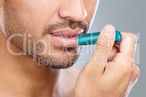 Vanquish dry lips. a man applying lip balm while standing against a grey background.