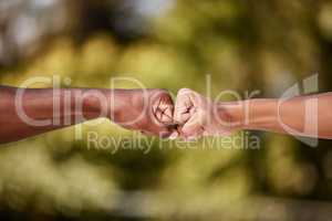 Fist bump of two interracial men outdoor against a blur background. Closeup of diverse athletes doing social gesture greeting in a park. Showing solidarity, friendship, brotherhood, teamwork or unity