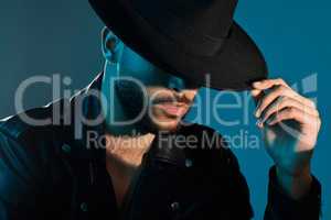 A hat completes the look. Conceptual shot of a stylish young man posing in studio against a blue background.