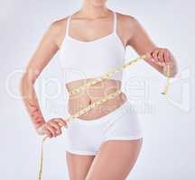 No extra inches for a perfect woman. Studio shot of an unrecognizable woman measuring her waist against a white background.