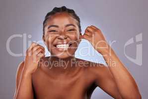 Flossing to reach all those in between spots. a young woman flossing her teeth while standing against a studio background.