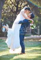 Full length shot of groom lifting his bride as they stand gazing into each others eyes. Loving newlywed couple in nature for wedding photo shoot