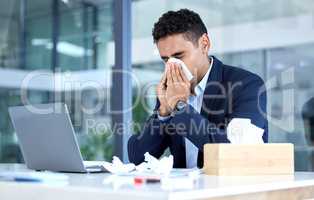 One sick mixed race business man blowing runny nose with tissue while working in an office. Hispanic guy feeling unwell with flu, cold and covid symptoms. Suffering with congestion, sinus and seasonal spring allergy