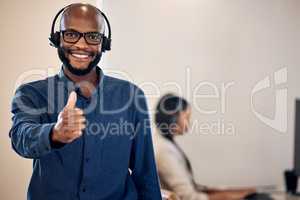 Good service is my guarantee. Portrait of a young call centre agent showing thumbs up in an office with his colleague in the background.