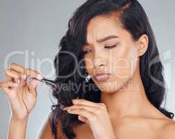 Dull hair days be gone. Studio shot of an attractive young woman looking upset while holding the ends of her hair against a grey background.