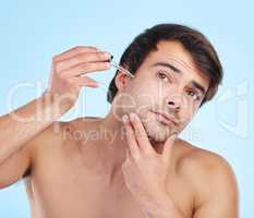 A solid routine is always worthwhile. a handsome young man applying a serum to his skin against a studio background.