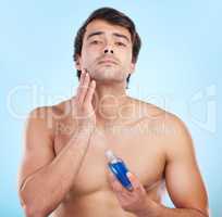 A great way to finish your routine. a young man applying cologne to his skin against a studio background.