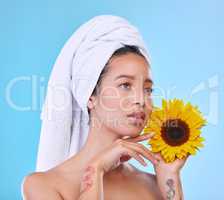 As bright and fresh as a sunflower. Studio shot of an attractive young woman posing with a towel on her head and a sunflower in her hand against a blue background.