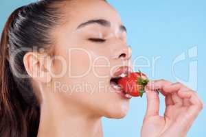 When you snack, snack healthy. Studio shot of an attractive young woman biting into a strawberry against a blue background.