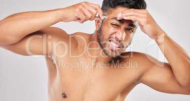 This is a struggle. a young man plucking his eyebrows against a grey background.