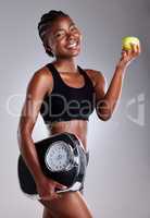 Diet and exercise can help keep you looking and feeling youthful. Studio portrait of a sporty young woman eating an apple while holding a scale against a grey background.