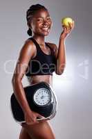 Diet and exercise are both important for optimal health. Studio portrait of a sporty young woman eating an apple while holding a scale against a grey background.