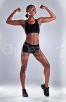 Look at how fabulous Ive gotten. Studio portrait of a sporty young woman flexing her arms against a grey background.