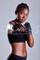 Shes more powerful than you think. Studio portrait of a sporty young woman wearing gloves and punching against a grey background.