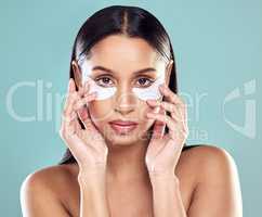 Keeping those wrinkles at bay. a young woman using eye masks against a studio background.