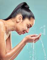 Time for the daily routine. a young woman washing her face and splashing water against a studio background.