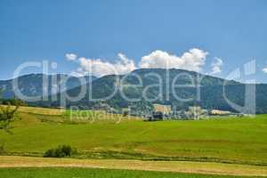 Farmland with lush meadow and hills or mountains covered with greenery in the countryside. Scenery of a calm empty field in nature. Natural view of open green landscape in the outdoors on a sunny day