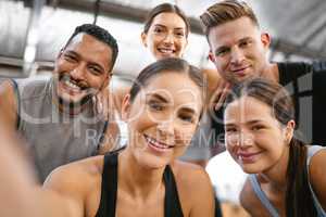 Portrait of a diverse group of happy sporty people taking selfies while exercising together in a gym. Cheerful motivated athletes excited and ready for training workout. Supportive friends taking photos for social media