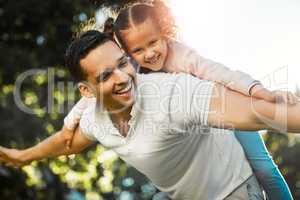 Cheerful father carrying daughter on his back. Little girl and daddy playing airplane. Child pretending to fly while getting piggyback ride at the park