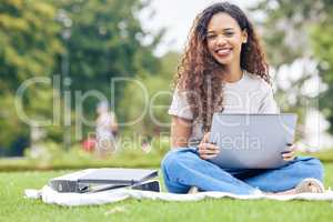 One young hispanic woman working on her laptop while sitting outside on an open field. A beautiful mixed race female student smiling while using her computer to study online on her university campus