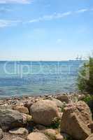 A calm quiet on the rocky beach coast of the Mediterranean ocean with the horizon and the intense illuminated blue sky with white clouds. A crystalline seascape with warm sunny weather during summer