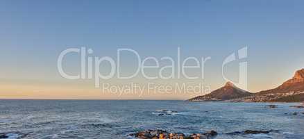 Ocean view of sea water on rocky beach, mountains and a blue sky with copy space of Lions Head in Cape Town, South Africa. Calm tide, serene and tranquil scenery of relaxing mother nature at sunrise