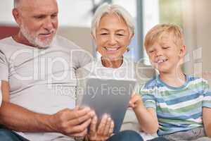 A happy mature couple bonding with their grandchild while babysitting and using a digital tablet on a couch at home. Grandparents relaxing with their cute little grandson and browsing the internet