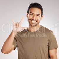 Handsome young mixed race man gesturing rock on while standing in studio isolated against a grey background. Hispanic male showing the sign language of I love you to show affection or romance