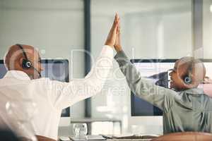 Two happy call centre telemarketing agents from the back giving each other high five and cheering with joy while working in an office. Excited and ambitious consultants celebrating successful sales targets and winning victory