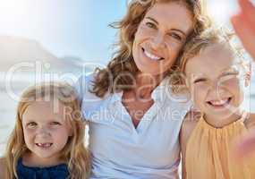 Portrait of a happy family taking a selfie at the beach while on a vacation in summer. Mature woman spending quality time with adopted or foster kids. Little girls on outing with their grandma