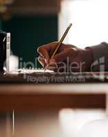 . Closeup of students hand using a pencil to write notes at a table. One clever guy studying for school, university or educational course. Learning and planning for exams, tests and academic lessons.