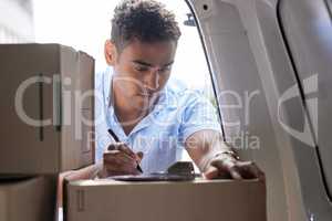 Organising his schedule for speedy deliveries. a young delivery man using a clipboard while checking boxes in a van.