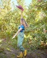 Cheerful farmer feeling optimistic and fulfilled for harvest season of fresh organic fruit. One excited energetic happy young woman jumping for joy on sustainable apple orchard farm on sunny day.