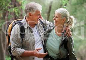 A senior caucasian couple smiling and looking happy in a forest during a hike in the outdoors. Man and wife showing affection and holding each other during a break in nature