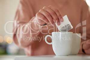 Ending my day with a hot cup of tea. a woman dropping a tea bag into a waiting mug.