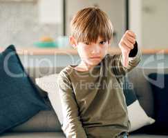 No kid enjoys being alone and hungry. Portrait of a cute little boy showing the thumbs down while sitting on a sofa at home.