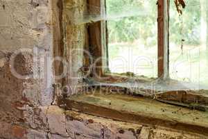 Interior view of an ancient house in need of TLC. An old window with dust and spiderwebs in an abandoned home inside. Architecture details of a windowsill frame with damaged rustic textures.