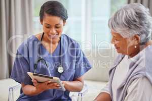 A hispanic senior woman in on a cosy sofa and her female nurse in the old age home and using a digital tablet. Mixed race young nurse and her patient talking in the lounge
