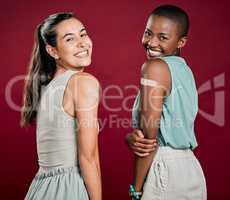 Covid vaccinated African american and mixed race women showing arm plaster. Portrait of two happy people isolated on red studio background with copyspace. Black woman and hispanic with corona vaccine