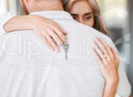 Closeup of happy wife hugging husband while holding keys after buying first home. Couple relocating to new house or apartment. Newlywed couple moving into their new place