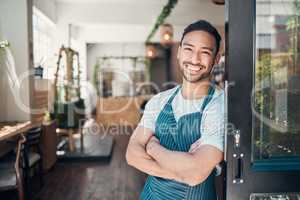Portrait of one happy young hispanic waiter standing with his arms crossed at the doorway of a store or cafe. Friendly man and coffeeshop owner managing a successful restaurant startup