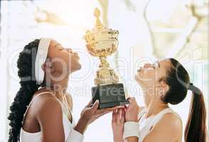 An award they worked hard for. two attractive young female tennis players kissing a trophy while standing in the clubhouse during their award ceremony.