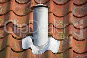 Closeup shot of a white steel chimney on an old brown tile roof outside. Stay warm this winter with a fireplace. Light a fire and get rid of the smoke quickly and conveniently. Every home needs one