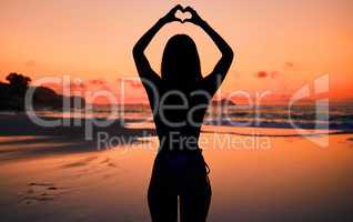 Love and the sky. an unrecognizable woman holding a heart with her hands above her head at the beach.
