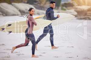 Surfing is almost a way to fly. Portrait of a young couple running towards the sea with their surfboards.