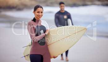 Its hot out and were looking to catch some waves. Portrait of a young woman surfing at the beach with her boyfriend in the background.