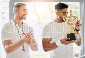 I cant think of anyone more deserving. a handsome young male tennis player kissing a trophy while his coach watches on and applauds.