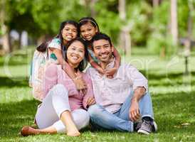 Portrait of happy asian family in the park. Adorable little girls bonding and hugging their parents outside in a park. Full length husband and wife sitting and enjoying free time with their daughters