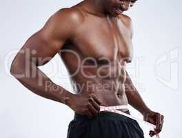 Dropping fat, picking up muscle. Studio shot of an unrecognizable musclar man measuring his waist against a grey background.