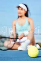 Pick up the ball and lets play. Full length shot of an unrecognisable woman sitting alone during tennis practice.